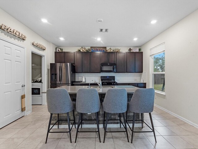 14203 Broad Cypress Ct, Houston, TX 77068 - kitchen with black microwave, stainless steel fridge, gas stove, backsplash, and a kitchen breakfast bar