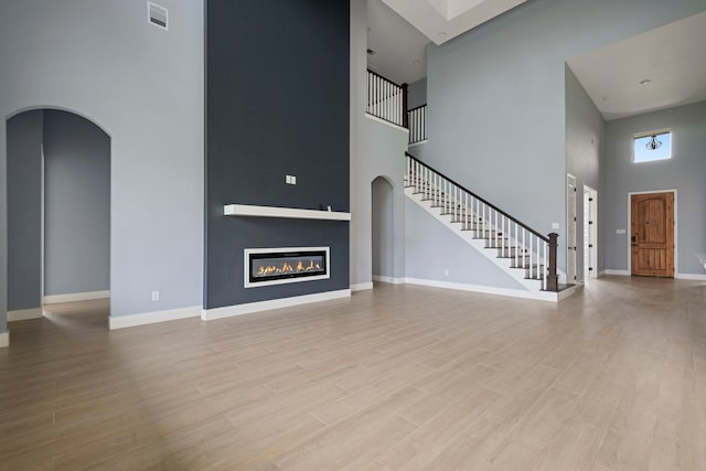 250 Hampton Glen Rd, Montgomery, TX 77356 - unfurnished living room featuring a high ceiling, arched walkways, wood finished floors, stairs, and baseboards