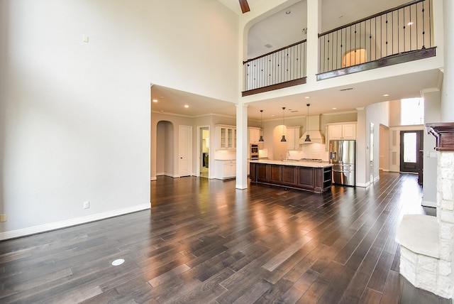 living room featuring a high ceiling, dark wood-style floors, arched walkways, and baseboards