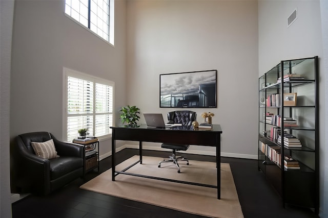 home office with healthy amount of natural light, wood finished floors, a towering ceiling, and baseboards