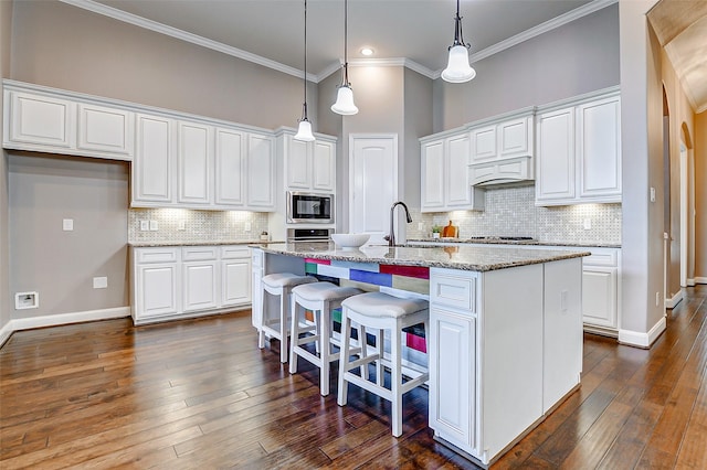 6315 Asbury Brook Ct, Katy, TX 77493 - kitchen featuring stainless steel microwave, white cabinetry, crown molding, a center island with sink, and baseboards