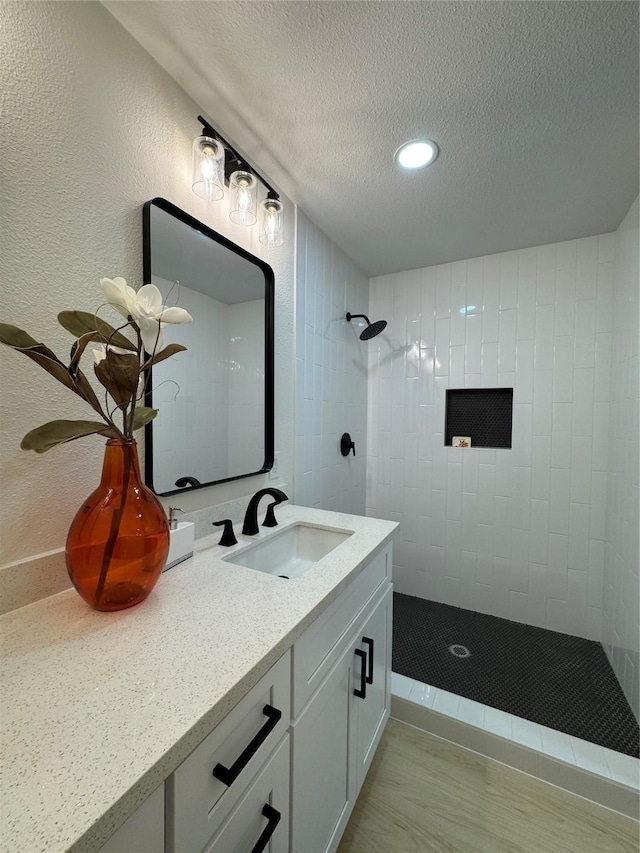 full bath with tiled shower, a textured ceiling, vanity, and recessed lighting