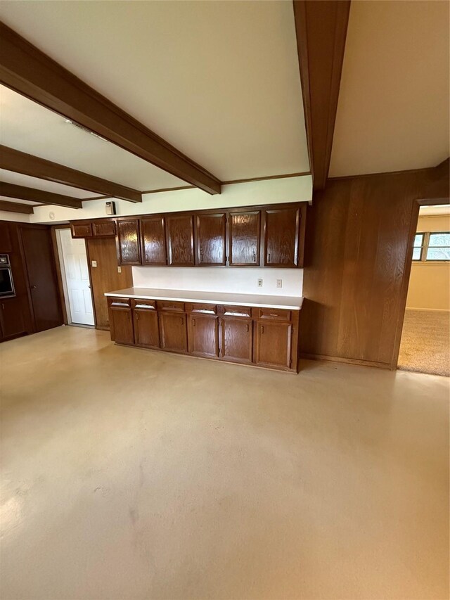 kitchen featuring beam ceiling, dark brown cabinets, light countertops, and wood walls
