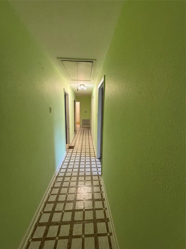 corridor with attic access, baseboards, a textured wall, and tile patterned floors