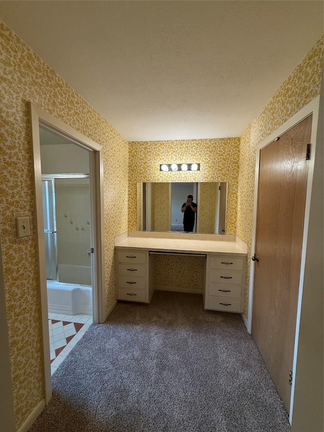 bathroom featuring wallpapered walls, carpet, vanity, bath / shower combo with glass door, and a textured ceiling