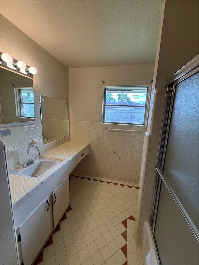 bathroom featuring a shower with shower door, tile patterned floors, a textured ceiling, vanity, and tile walls