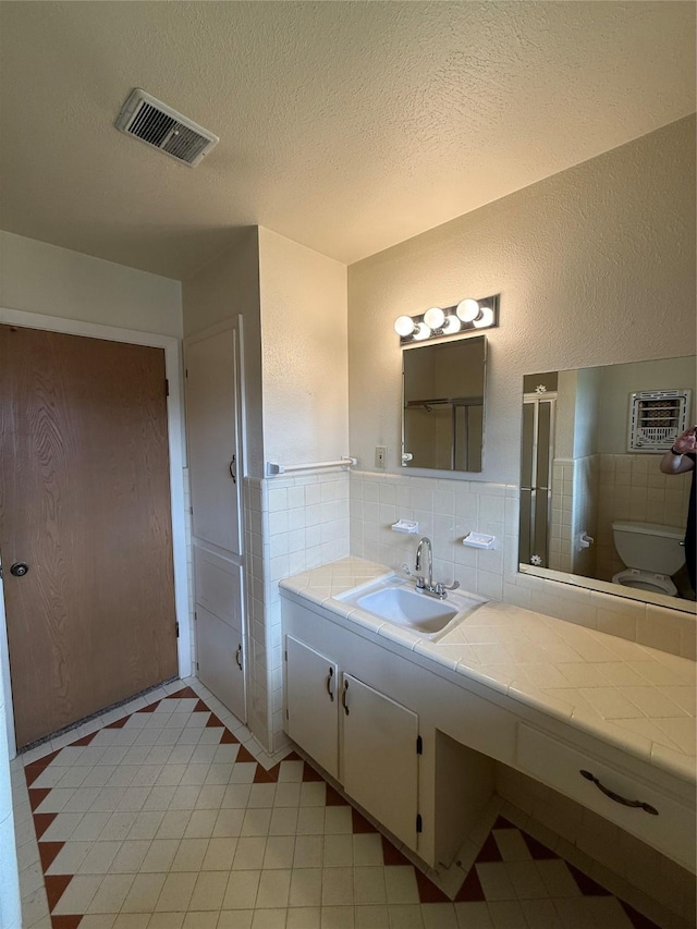 full bathroom featuring toilet, vanity, tile patterned floors, a textured ceiling, and tile walls