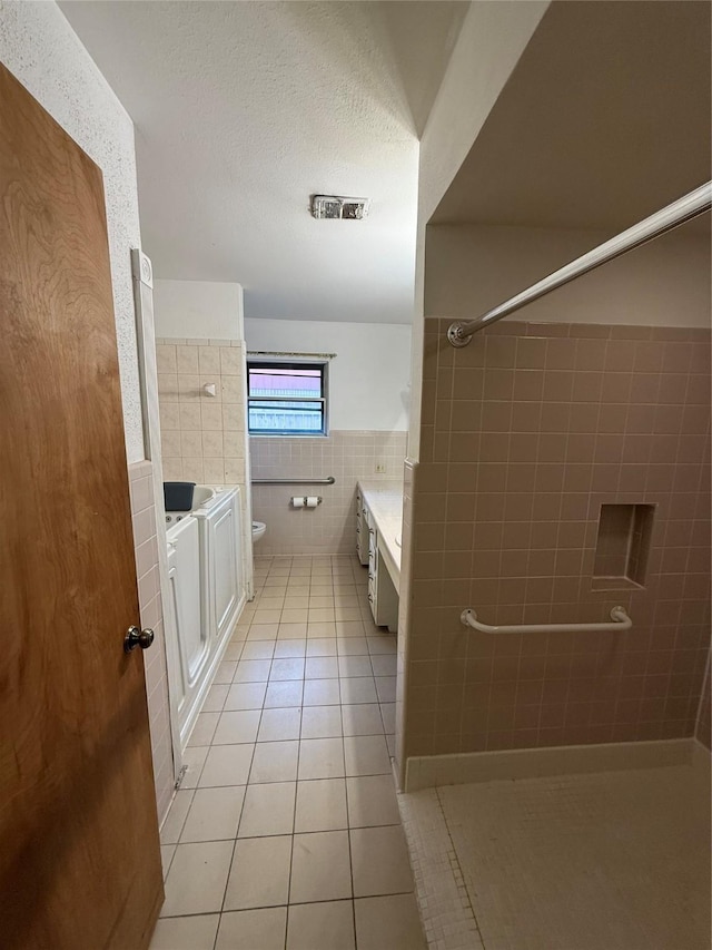 bathroom featuring tile walls, tile patterned floors, toilet, vanity, and a shower