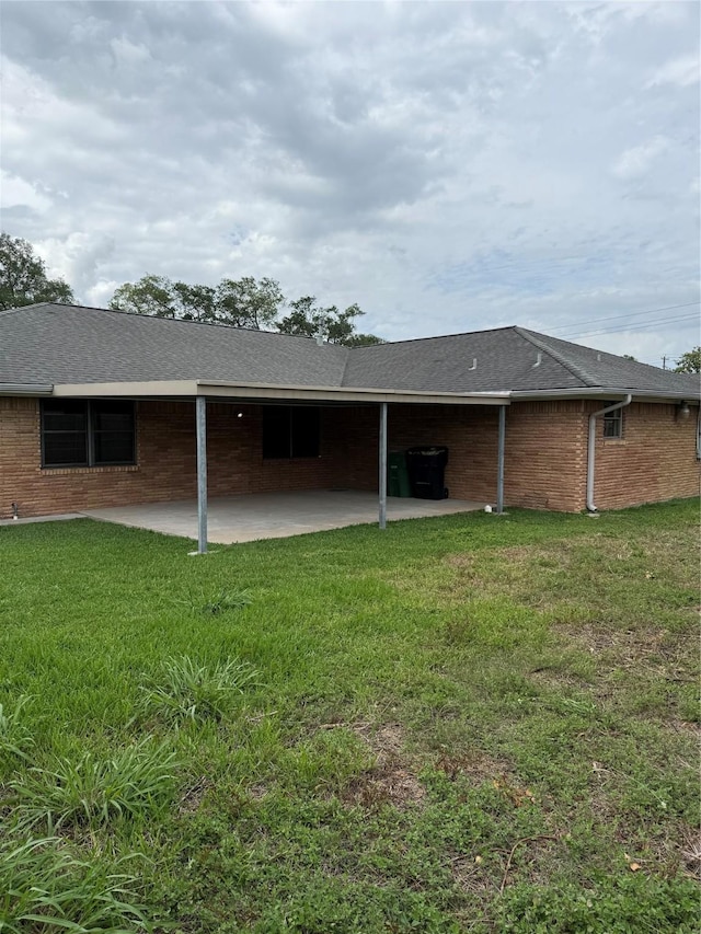 rear view of house with a patio, a yard, brick siding, and roof with shingles