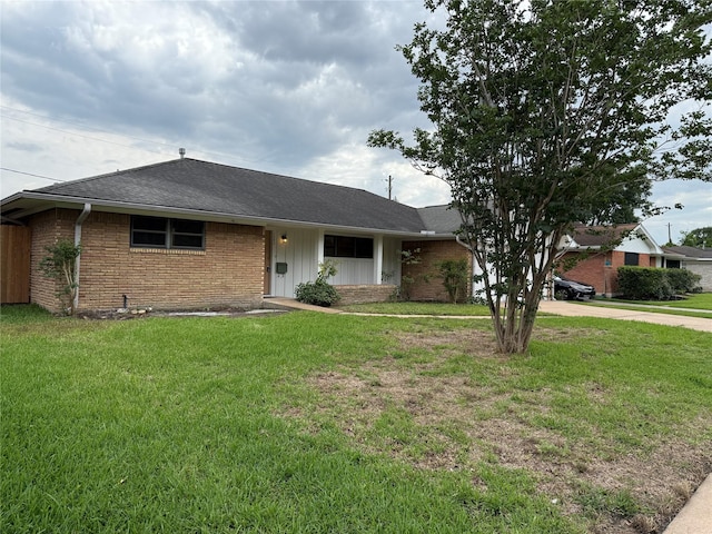 view of front facade featuring brick siding, a front lawn, a shingled roof, and driveway