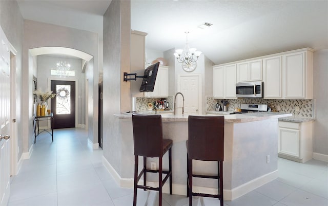 13931 Pueblo Run, Cypress, TX 77429 - kitchen featuring stainless steel microwave, a chandelier, stove, arched walkways, and lofted ceiling