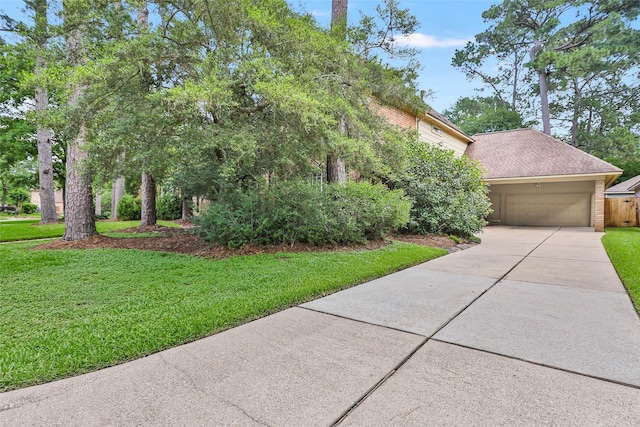 view of property hidden behind natural elements featuring a garage, a front yard, concrete driveway, and a shingled roof