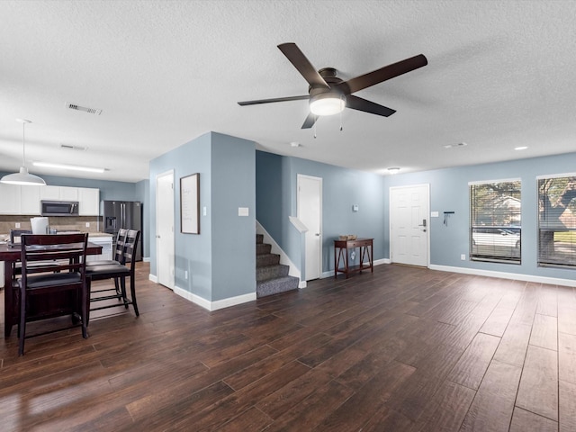living area featuring a ceiling fan, dark wood finished floors, stairs, a textured ceiling, and baseboards