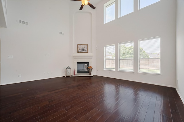 4142 Regal Stone Ln, Sugar Land, TX 77479 - unfurnished living room with a towering ceiling, a ceiling fan, a glass covered fireplace, dark wood-style floors, and baseboards