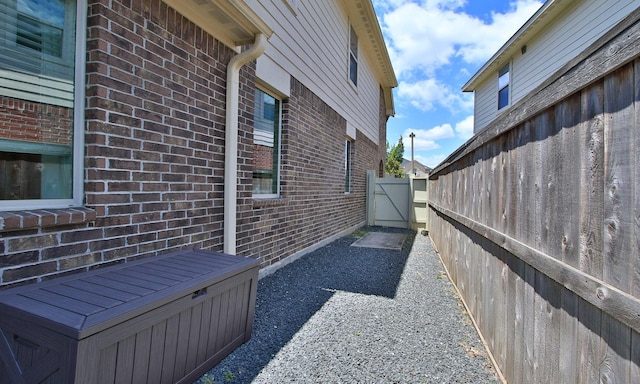 view of side of home featuring brick siding, a gate, and fence