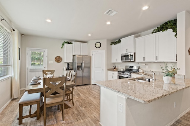 kitchen with stainless steel appliances, a sink, light wood-style flooring, light stone counters, and a peninsula