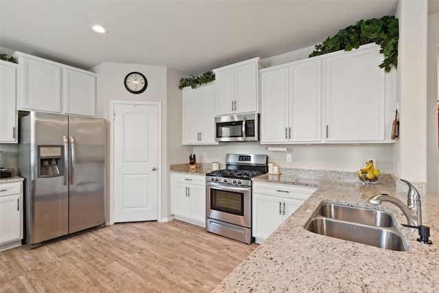 kitchen with appliances with stainless steel finishes, a sink, white cabinetry, light wood-type flooring, and light stone counters