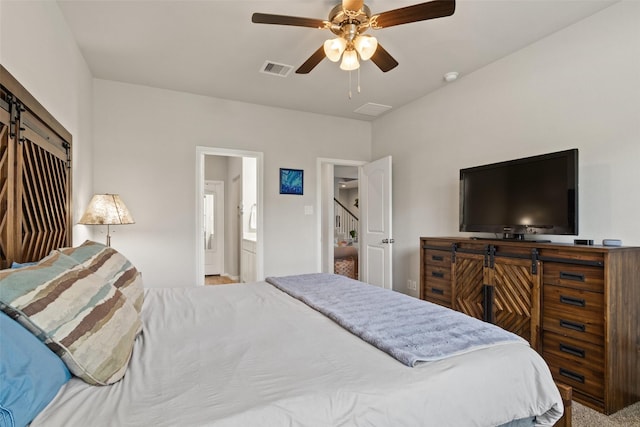 bedroom with a barn door, a ceiling fan, ensuite bath, and carpet flooring