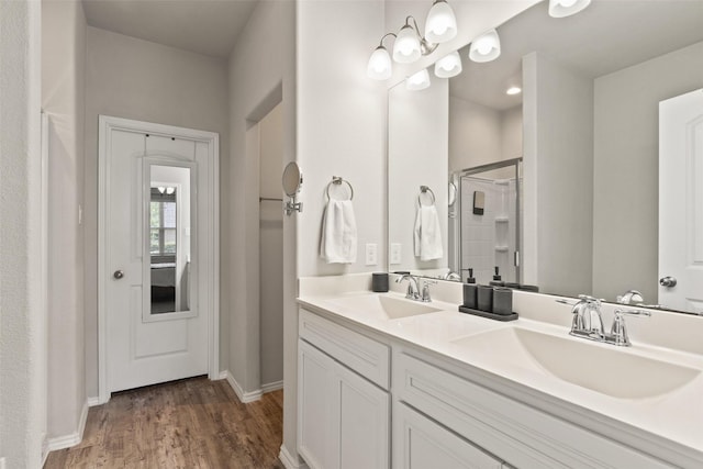 bathroom with a shower stall, wood finished floors, baseboards, and double vanity
