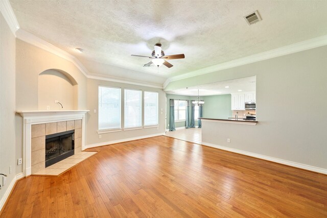 13313 Enchanted Way Dr, Montgomery, TX 77356 - unfurnished living room featuring ceiling fan, a tile fireplace, light wood-style flooring, a chandelier, and ornamental molding