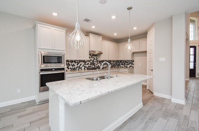 kitchen with appliances with stainless steel finishes, a sink, light wood-style flooring, backsplash, and recessed lighting