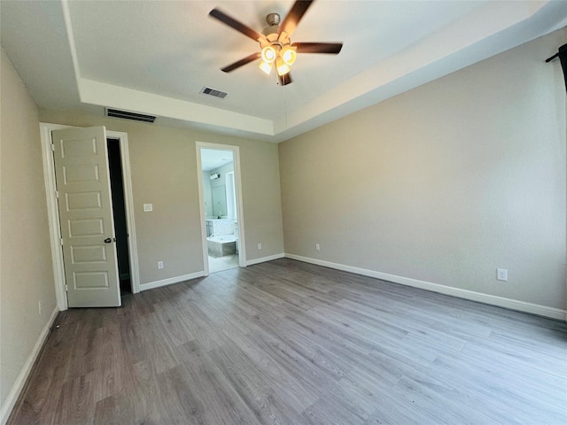 spare room with a raised ceiling, ceiling fan, wood finished floors, and baseboards