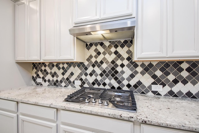 kitchen featuring under cabinet range hood, stainless steel gas stovetop, white cabinetry, decorative backsplash, and light stone countertops
