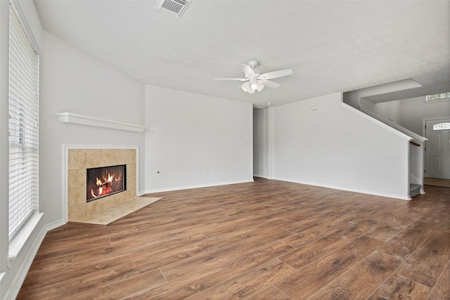 unfurnished living room featuring wood finished floors, a ceiling fan, a tile fireplace, and stairs