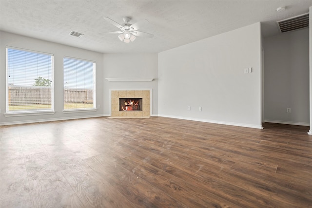 unfurnished living room with a ceiling fan, dark wood-style flooring, baseboards, a tiled fireplace, and a textured ceiling