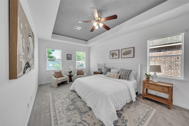 bedroom featuring light colored carpet, a tray ceiling, baseboards, and a ceiling fan