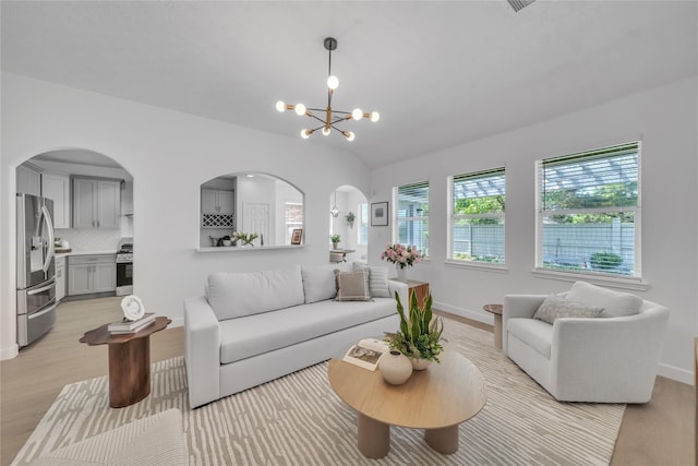 living room with arched walkways, light wood-style floors, a chandelier, vaulted ceiling, and baseboards