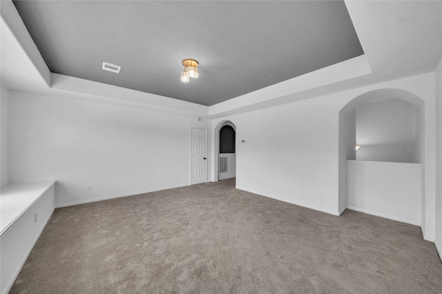 carpeted empty room featuring a raised ceiling and arched walkways