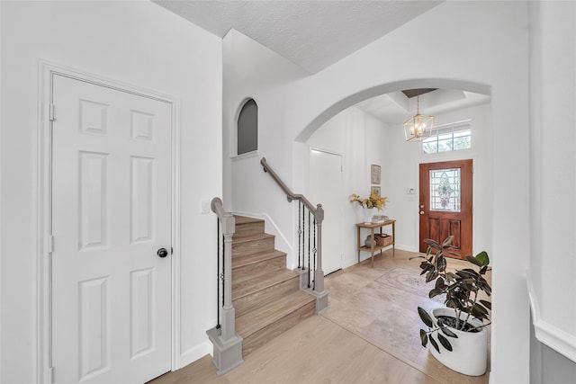 entrance foyer featuring arched walkways, light wood-type flooring, stairs, and a chandelier