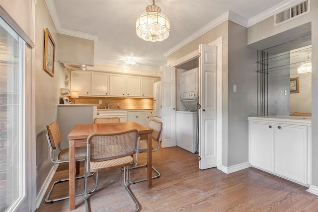 dining space with stacked washer / dryer, wood finished floors, a chandelier, baseboards, and crown molding