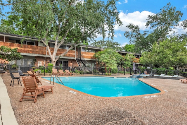 community pool featuring fence, a patio, and stairway