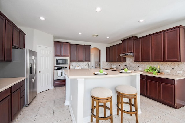 5530 Riverstone Crossing Dr, Sugar Land, TX 77479 - kitchen with appliances with stainless steel finishes, decorative backsplash, light tile patterned flooring, a center island with sink, and recessed lighting