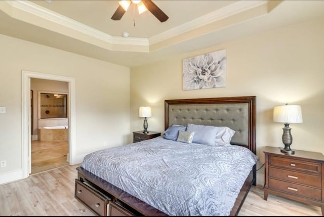 bedroom with light wood-style floors, a tray ceiling, crown molding, ensuite bathroom, and baseboards