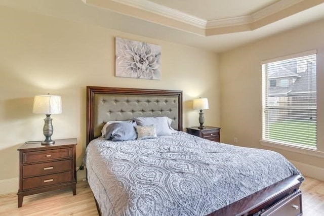 bedroom with crown molding, light wood-type flooring, and a raised ceiling