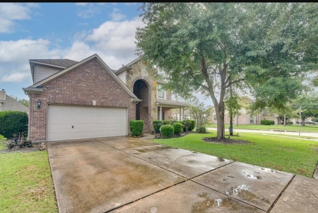 view of front facade featuring brick siding, a front yard, an attached garage, and driveway
