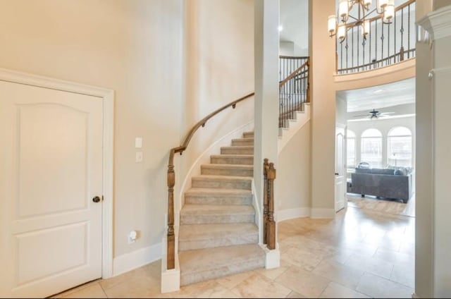 stairs with a chandelier, a towering ceiling, ceiling fan, and baseboards