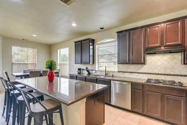 kitchen featuring appliances with stainless steel finishes, a sink, backsplash, under cabinet range hood, and a kitchen island