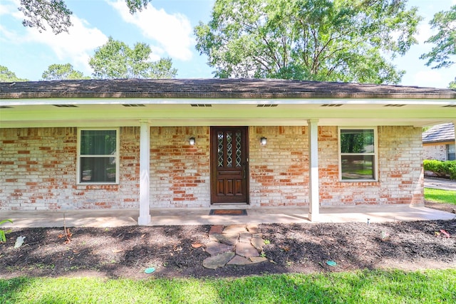 doorway to property with a porch and brick siding