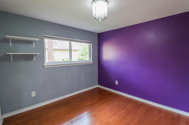spare room with wood finished floors, a chandelier, and baseboards
