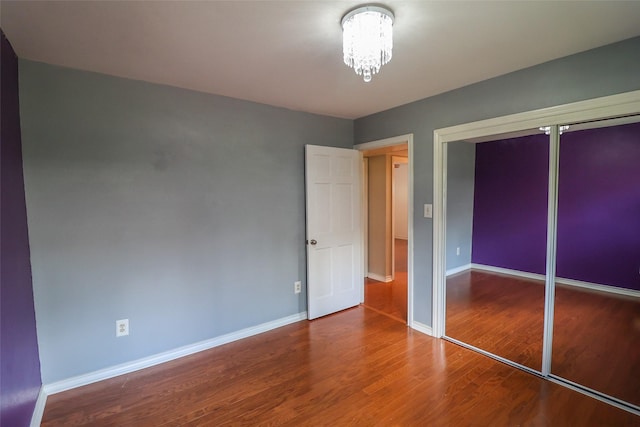 unfurnished bedroom with wood finished floors, a chandelier, baseboards, and a closet