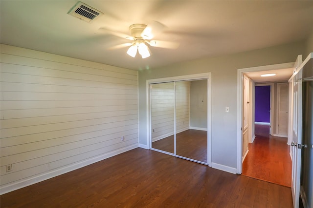 unfurnished bedroom with dark wood finished floors, a closet, baseboards, and ceiling fan