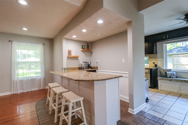 kitchen featuring a textured ceiling, a breakfast bar, light stone counters, a peninsula, and baseboards