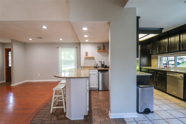 kitchen featuring stainless steel dishwasher, a breakfast bar area, a sink, light stone countertops, and a peninsula
