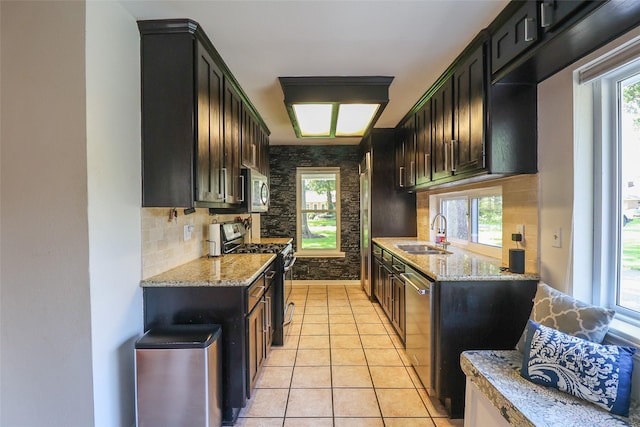 kitchen with stainless steel appliances, a sink, light stone counters, and backsplash