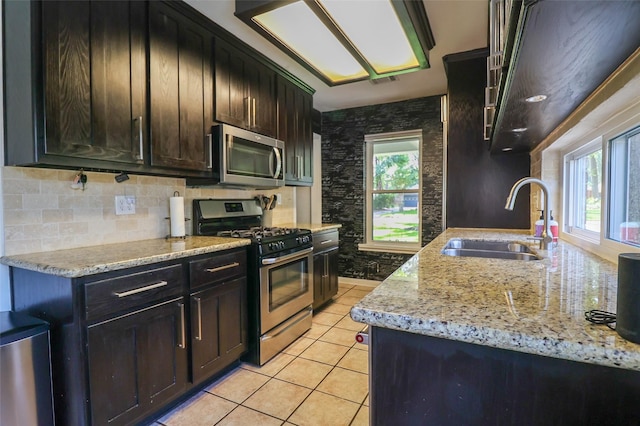 kitchen featuring stainless steel appliances, a sink, light tile patterned flooring, light stone counters, and tasteful backsplash