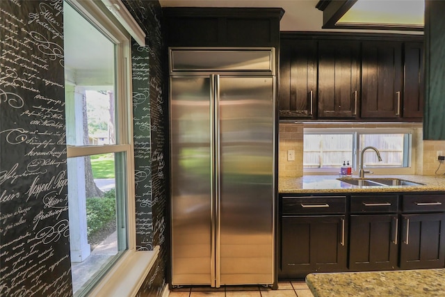 kitchen with stainless steel built in refrigerator, a sink, backsplash, and light stone counters